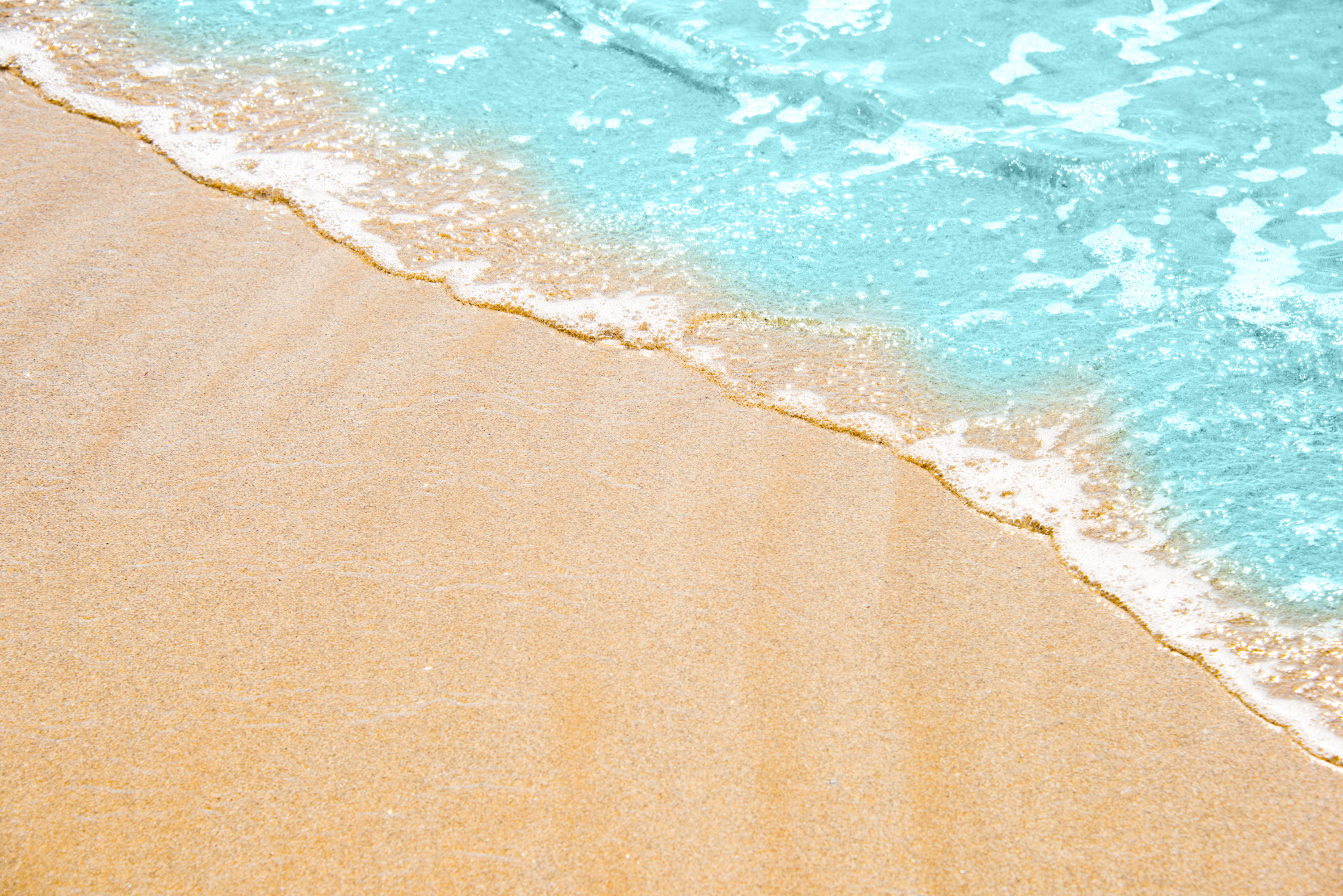 Soft wave of turquoise sea water on the sandy beach. Close-up and directly above photographed.