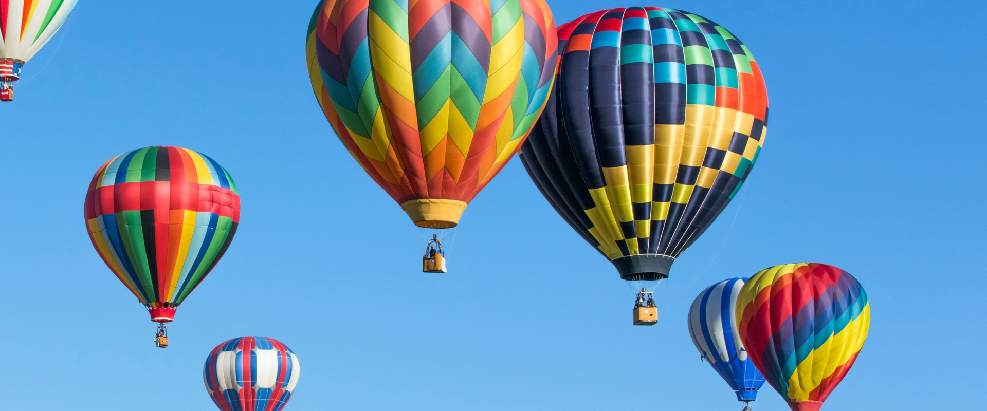 Colourful hot air balloons are rising up on the blue sky. Picture is taken from a distanced hot air balloon.
