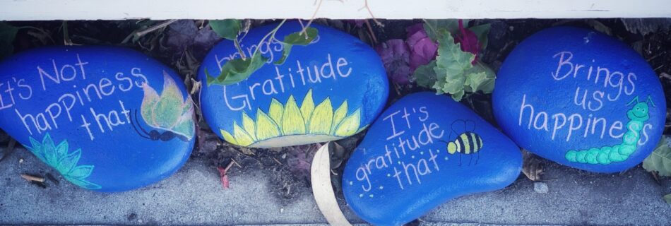 Blue painted beach rocks with images and words on them. The words are 'It's not happiness that brings Gratitude. It's gratitude that brings us happiness.