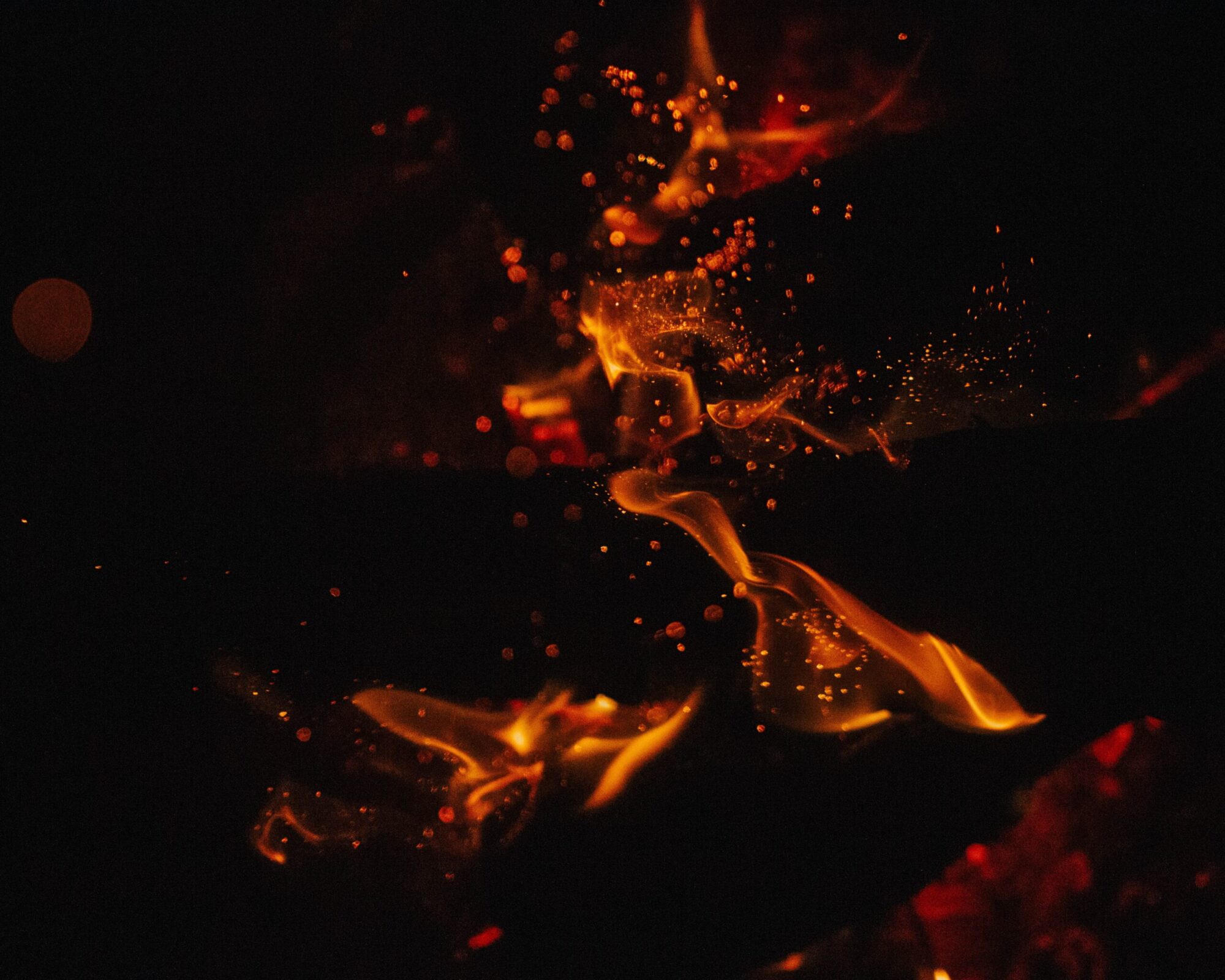 Black background warm yelllow and red flames and sparks are going up in the sky.