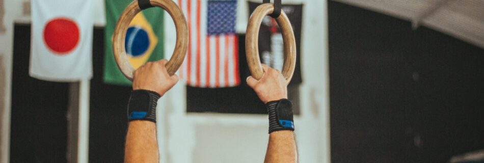 Male gymnast's arms on the rings. And countries flags in the background.